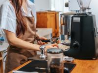 Ung kvinde arbejder ved espresso-maskine