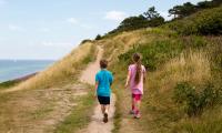 En dreng og en pige går i bakket landskab nær stranden i solskin